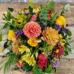 Autumn floral arrangement with a coral dahlia, orange chrysanthemums, and yellow roses on a rustic wood table at The Truffle Farm