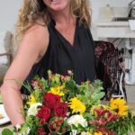 A workshop guest holding a fall arrangement of red roses, sunflowers, and seasonal blooms at The Truffle Farm