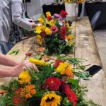 Workshop guests arranging fall floral centrepieces with sunflowers, zinnias, and dahlias on the long table at The Truffle Farm